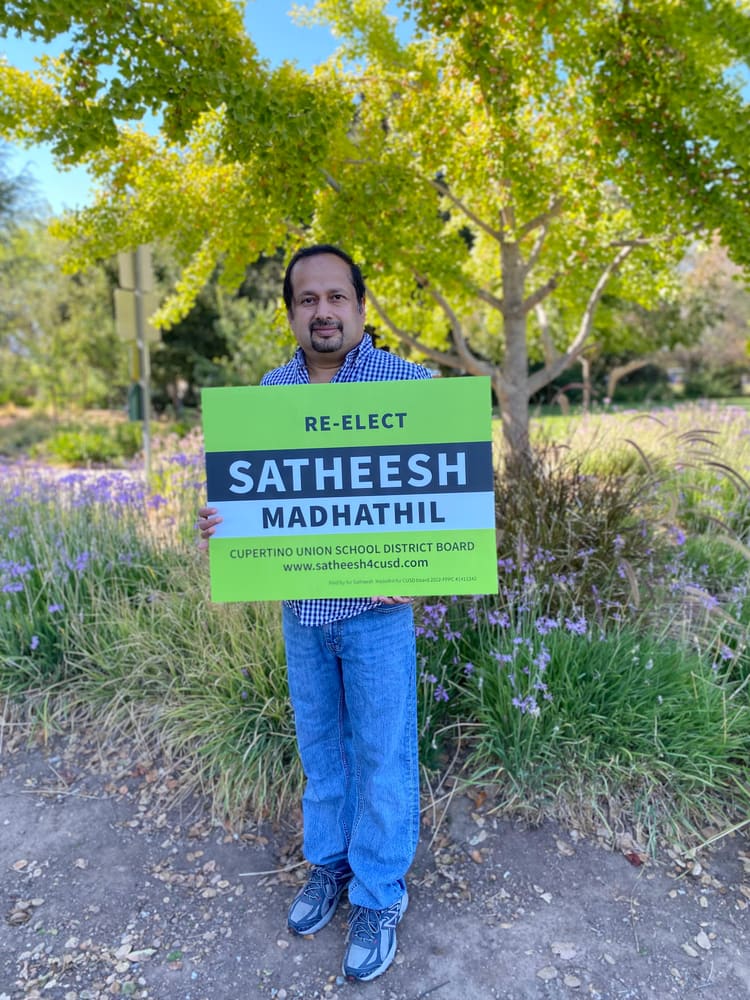 Satheesh Madhathil holding a Re-elect Satheesh Madhathil campaign yard sign