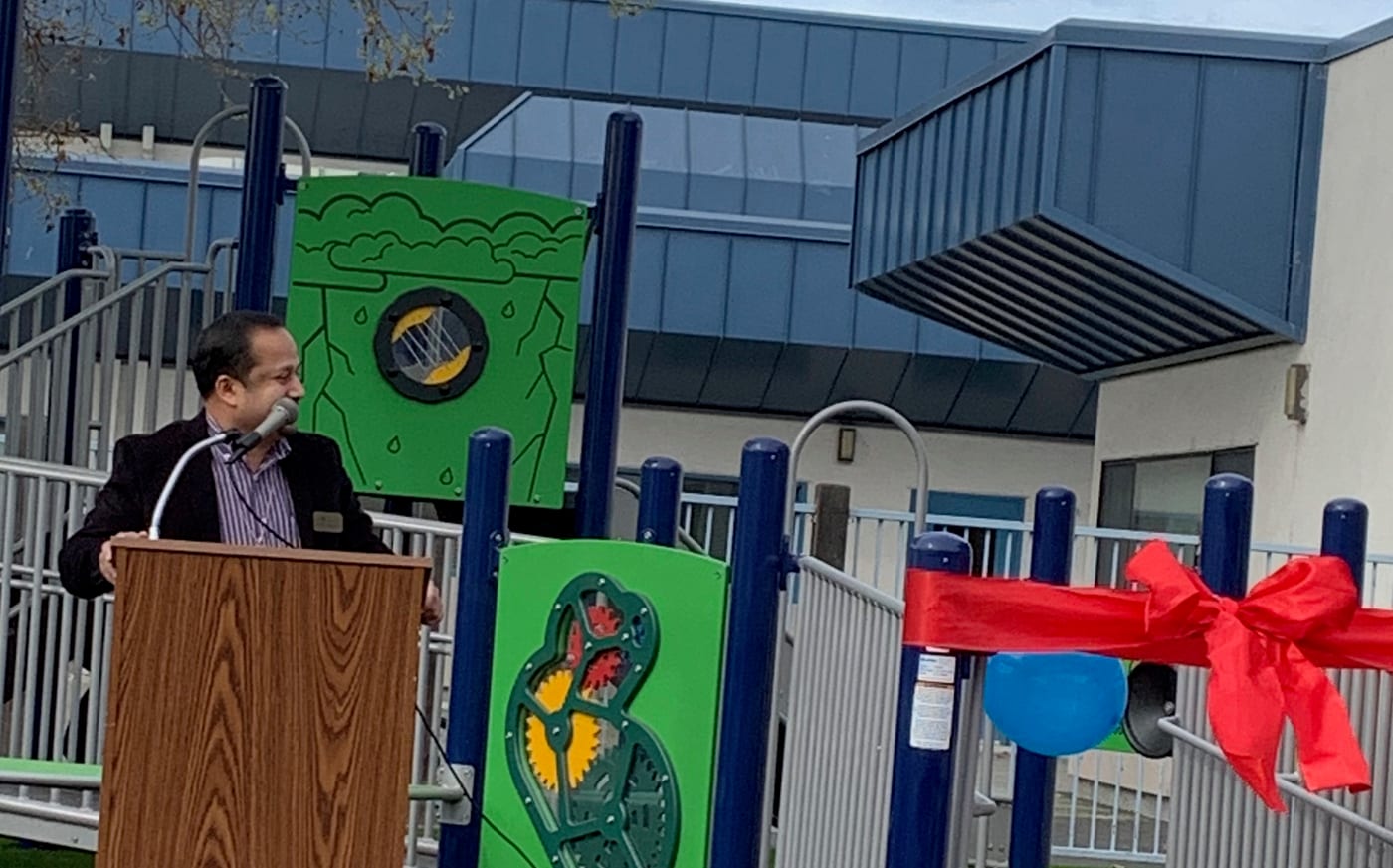 Satheesh Madhathil speaking at a podium during the opening of a new school playground